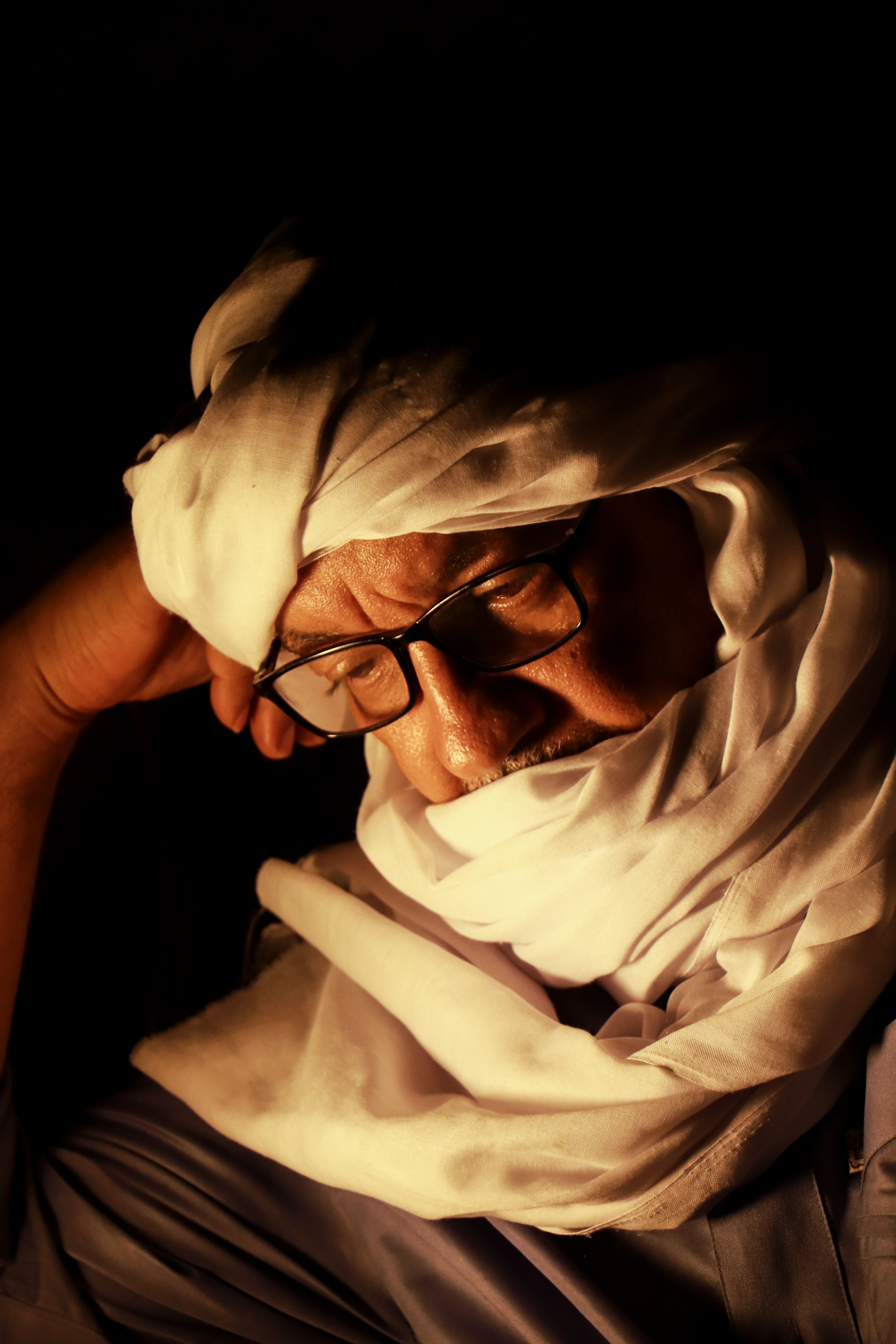 Portrait of an elderly man wearing glasses and traditional white turban, lost in thought.