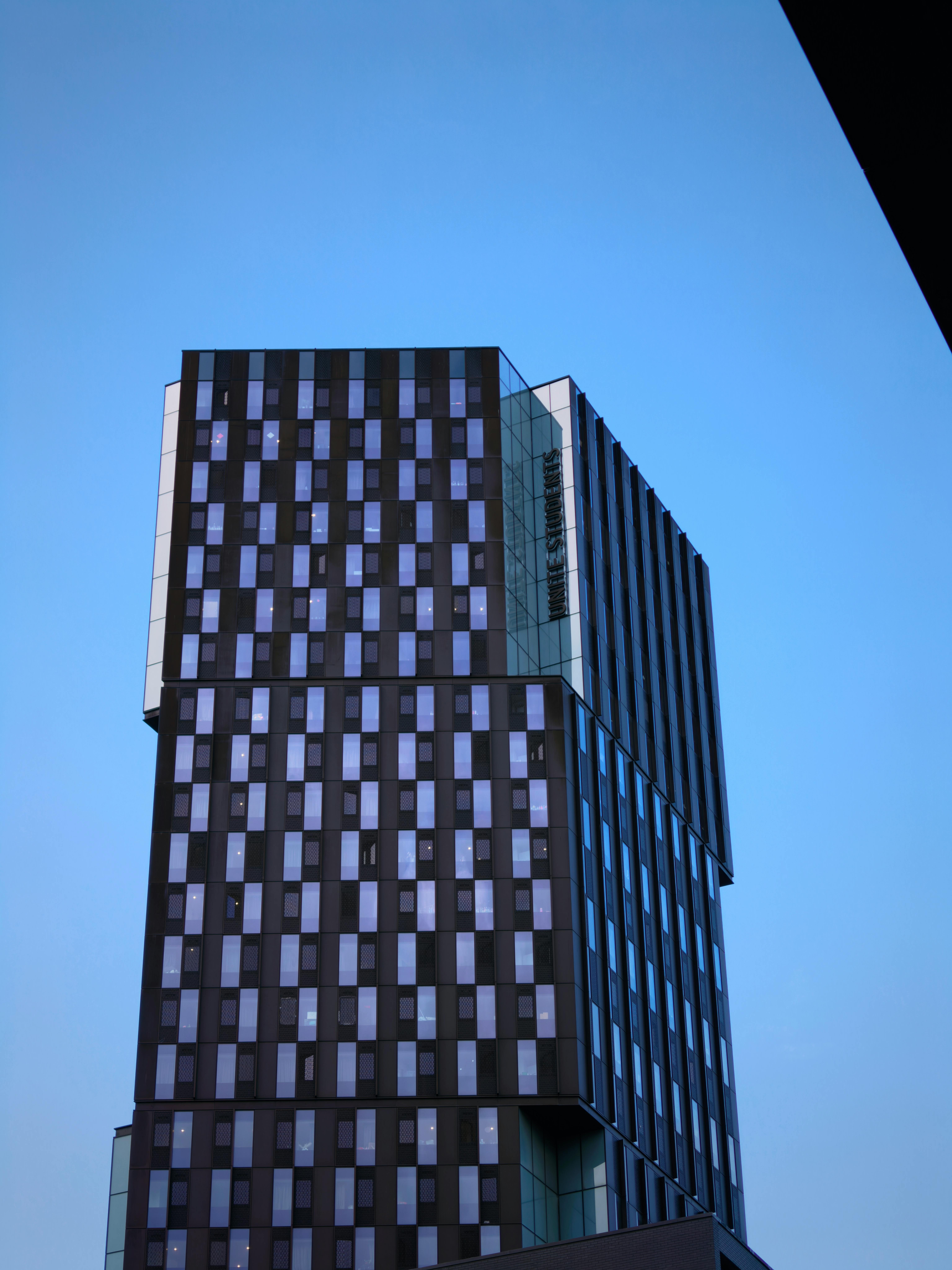 Gratuit O clădire elegantă, cu un design geometric, se înalță sub un cer albastru senin, etalând o arhitectură modernă. Fotografie de stoc