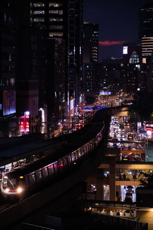 Free Vibrant cityscape at dusk with a train cutting through illuminated skyscrapers and bustling street lights. Stock Photo