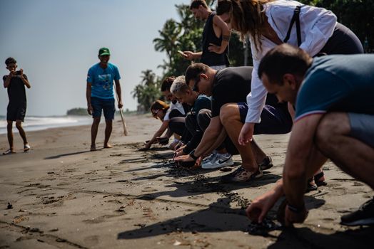 A group of adults participating in a beach cleanup activity on a sunny day in Bali, Indonesia.