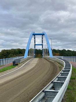 Photo of a blue arched bridge with symmetrical design over a dirt path.