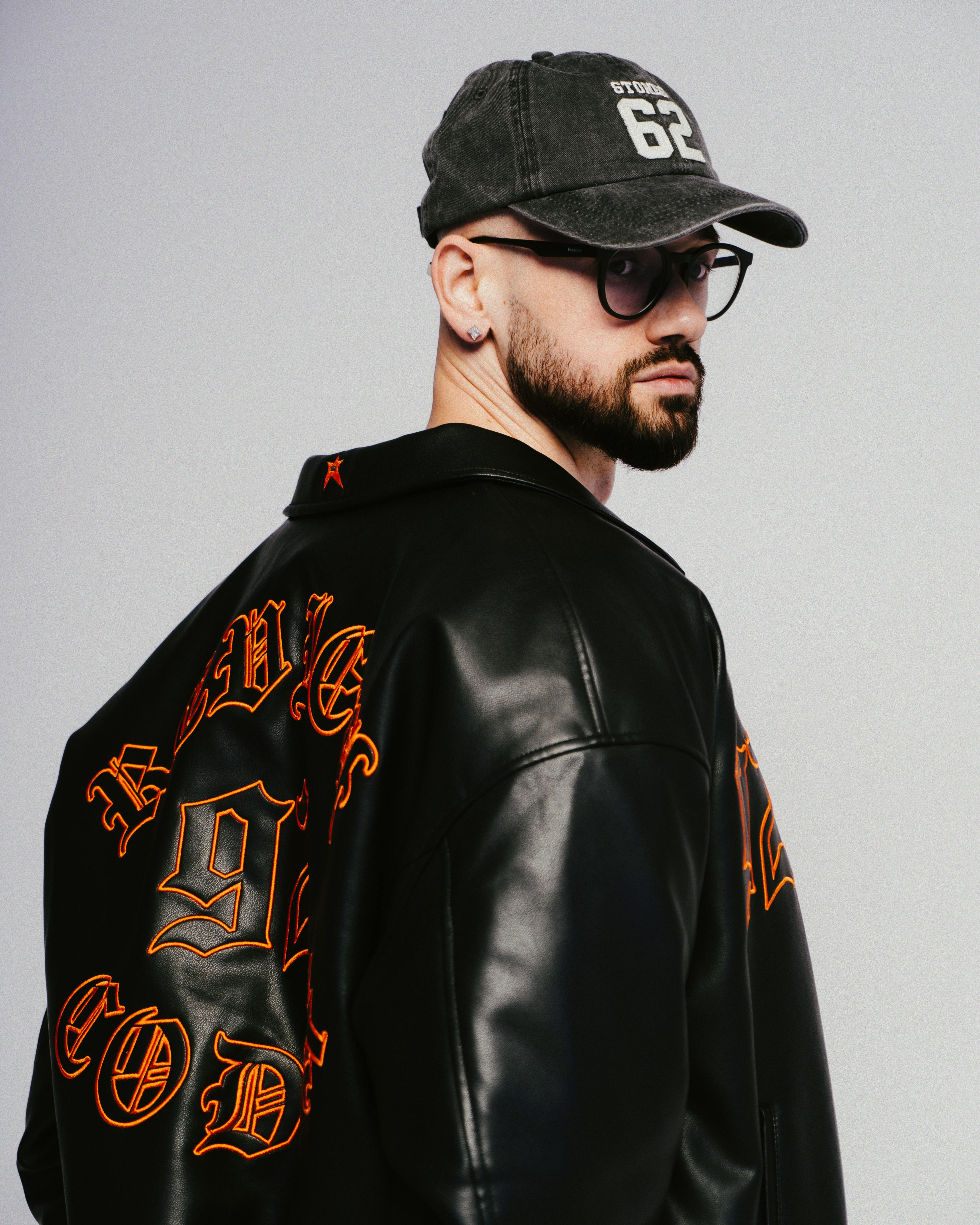 Man wearing a leather jacket and a cap, presenting urban street style fashion.