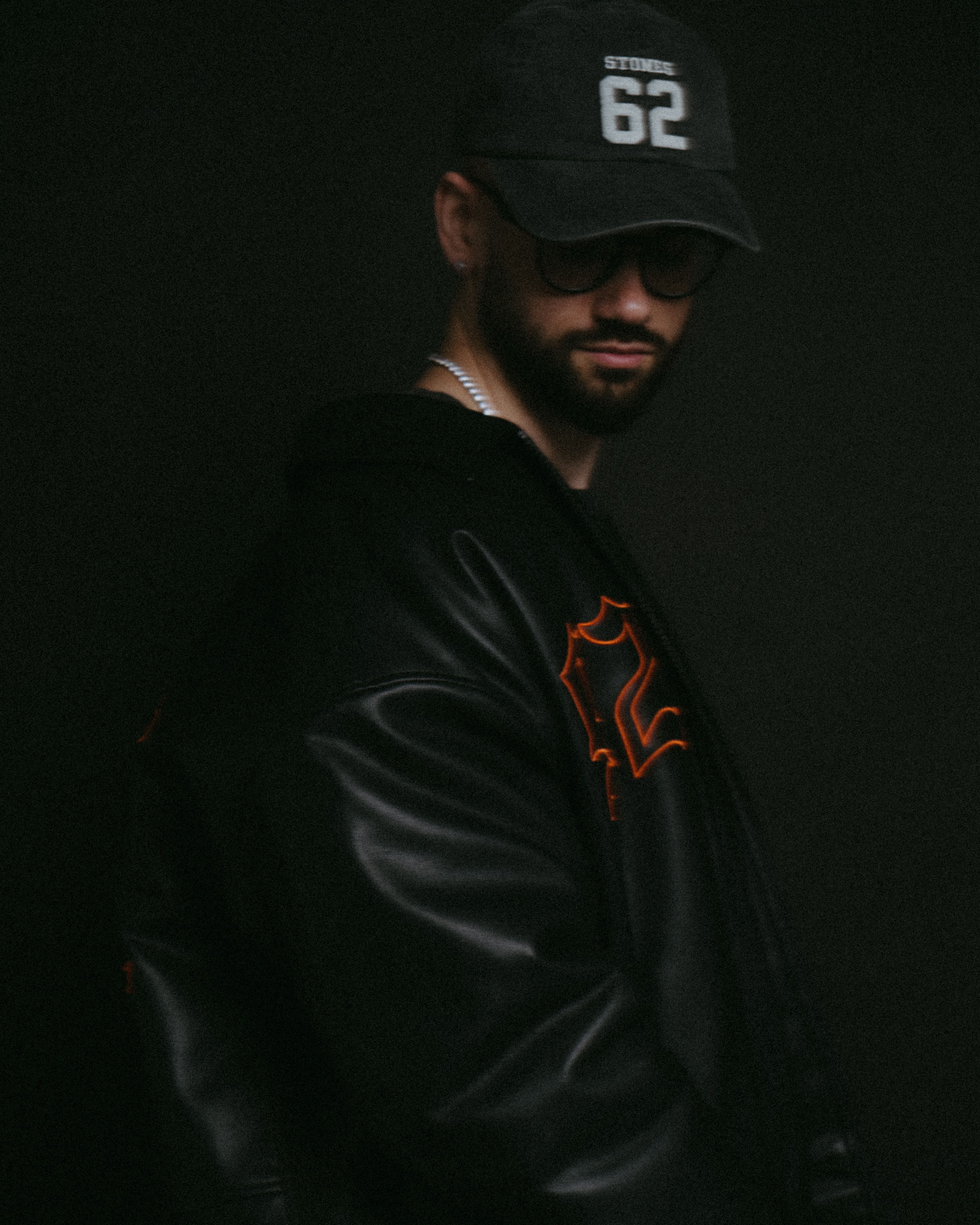 Stylish man wearing a leather jacket and hat against dark background.