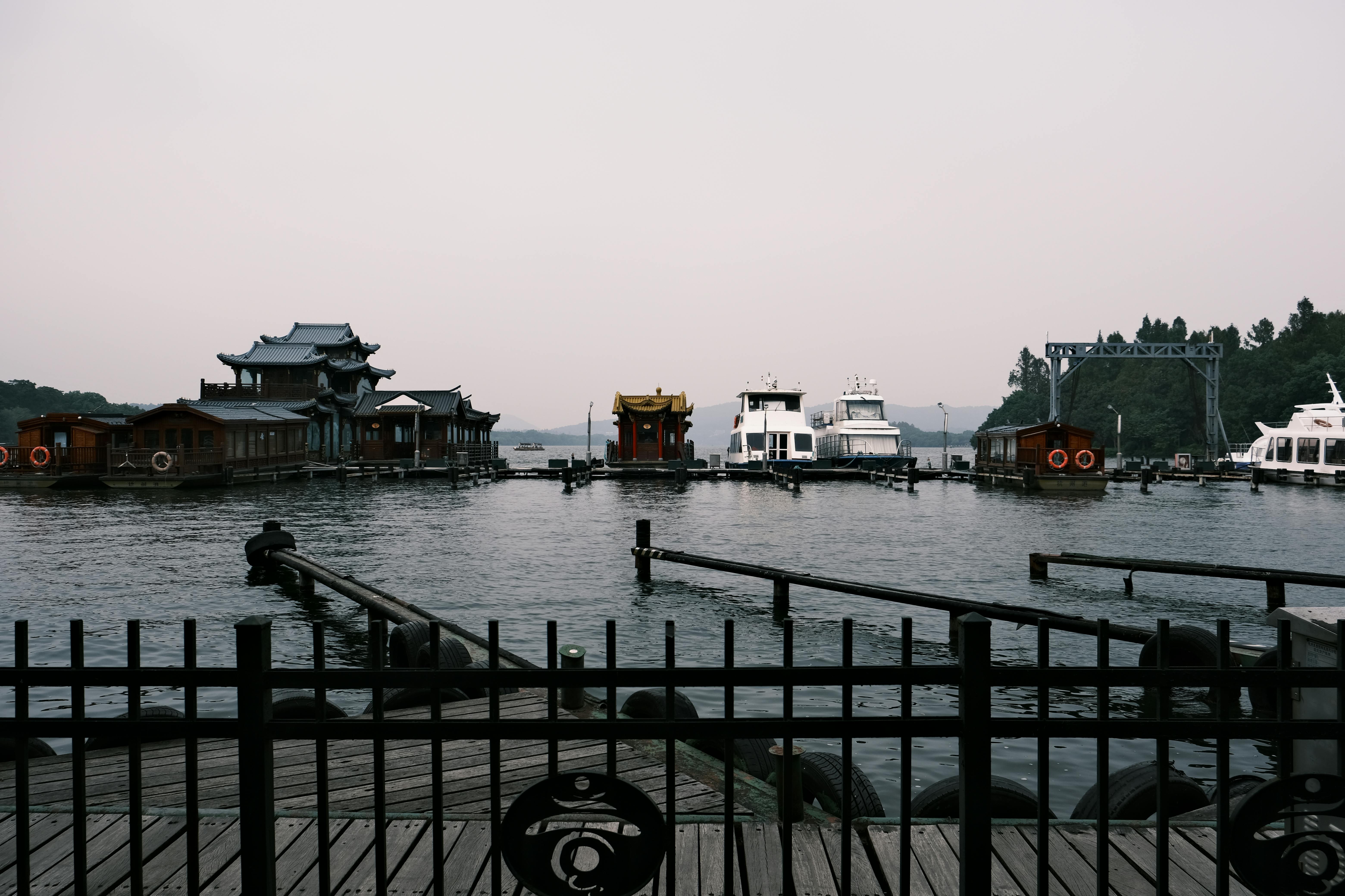 Serene view of historic boats and structures on West Lake in Hangzhou, China, with misty mountains.