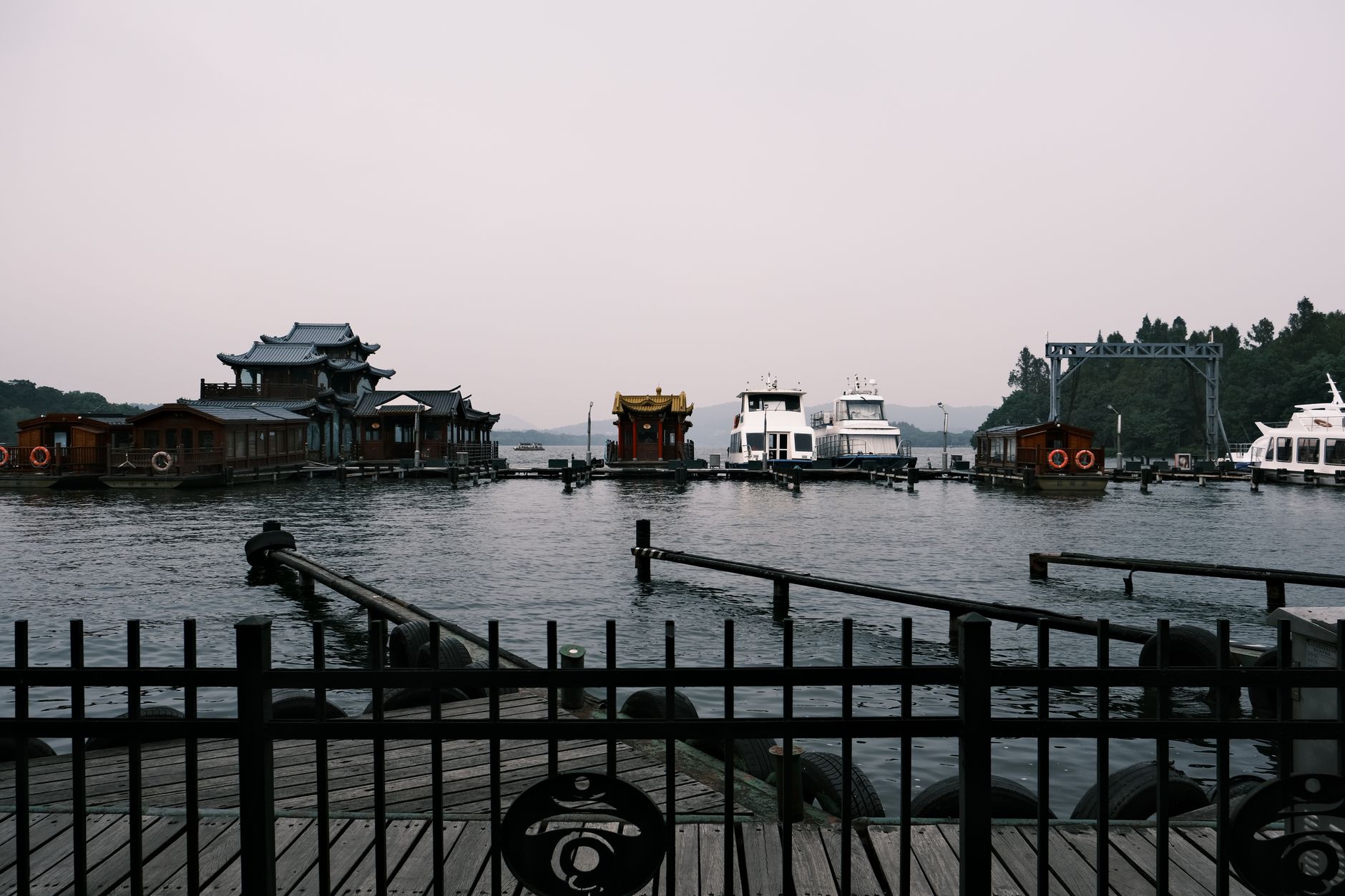 Serene view of historic boats and structures on West Lake in Hangzhou, China, with misty mountains.