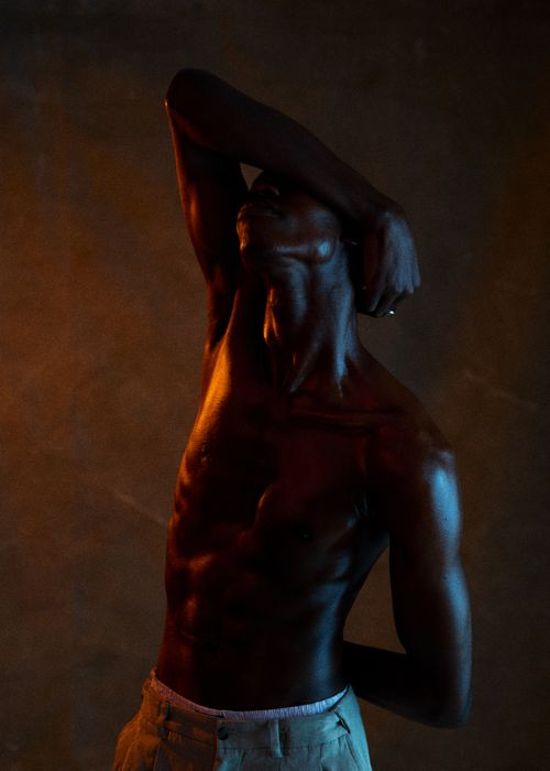 Free Artistic low-light portrait of a muscular black man in a contemplative pose. Stock Photo