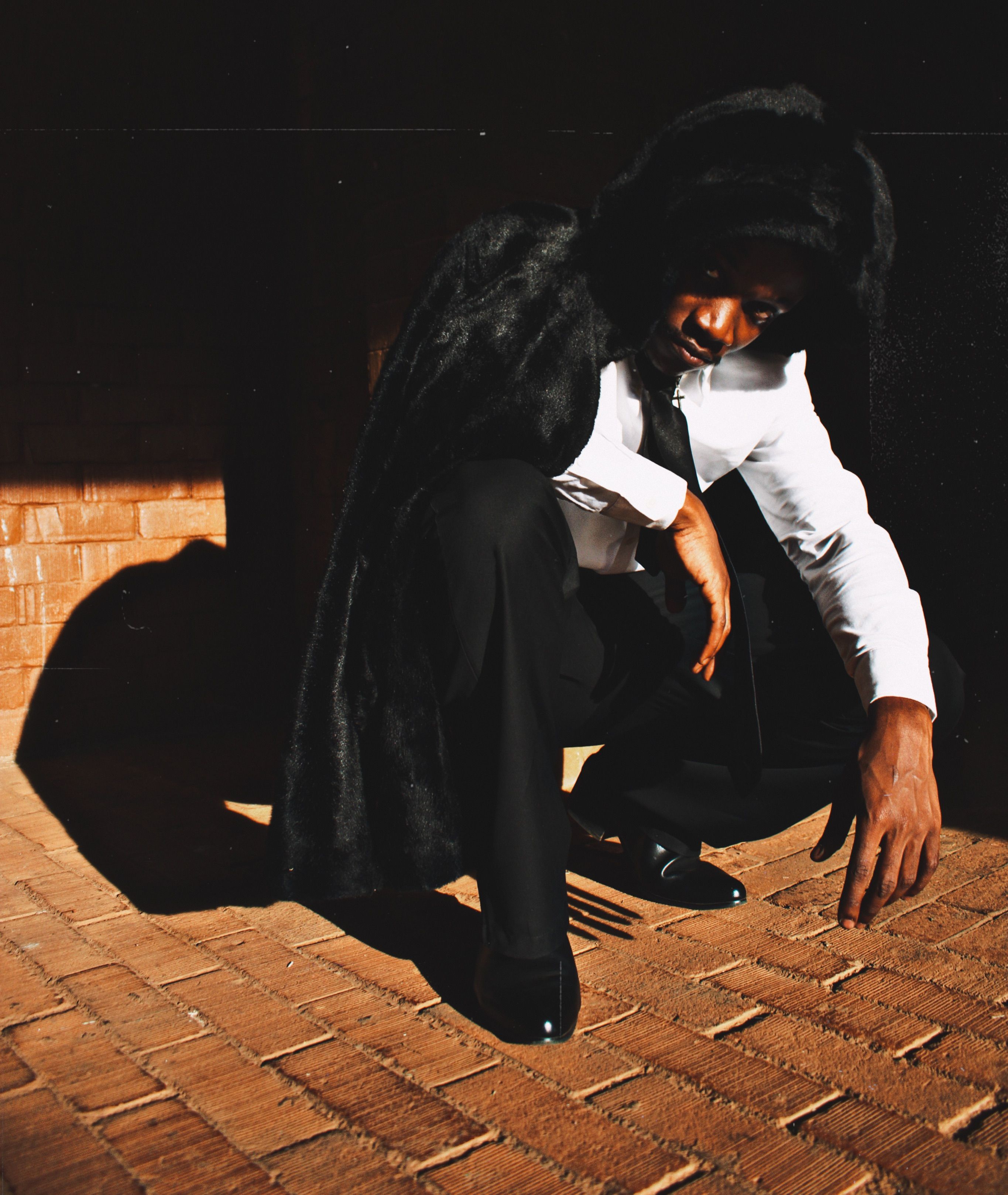 A person dressed in formal attire posing in shadow and light on a brick floor.