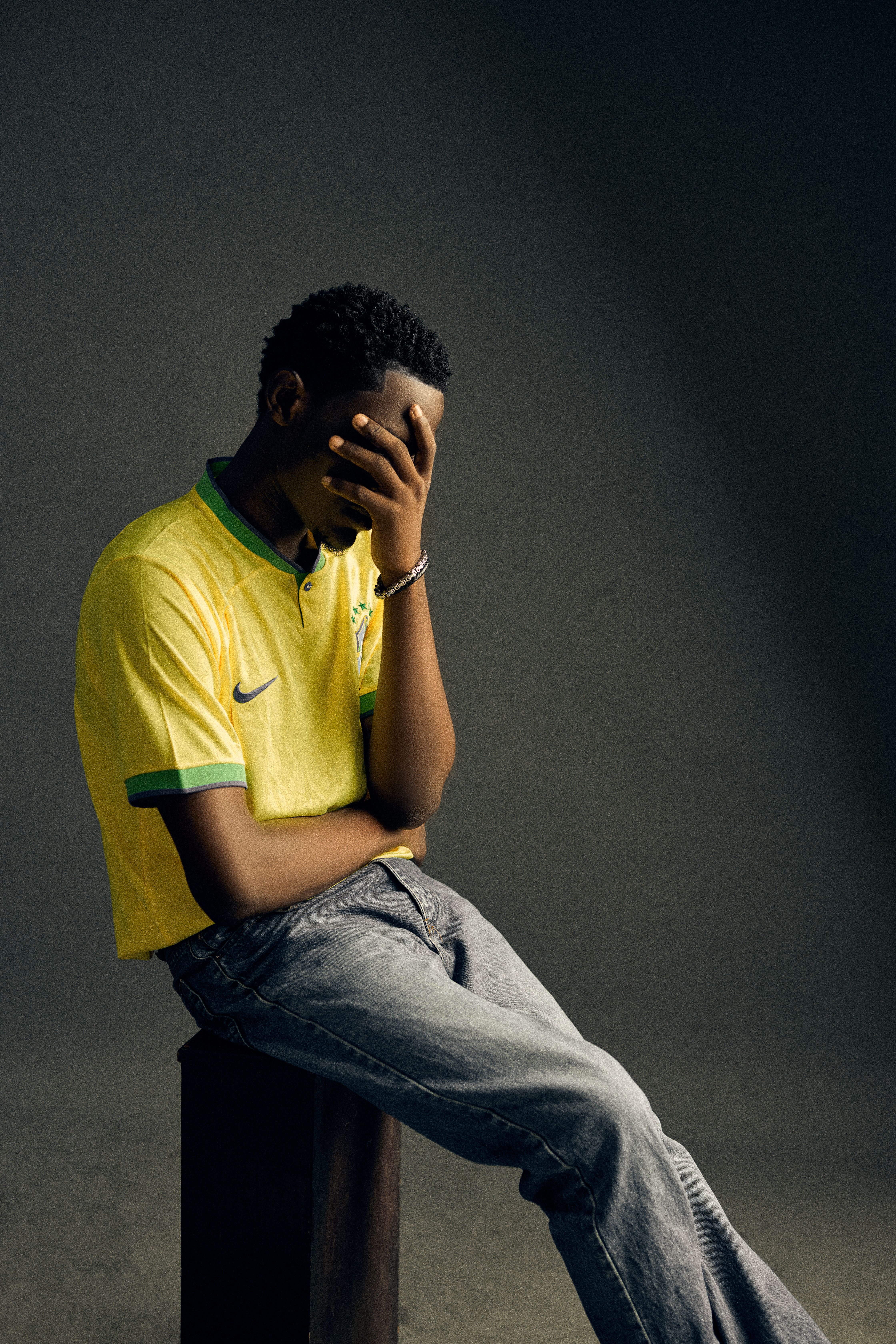 A young man wearing a yellow sports jersey sits thoughtfully with his face in his hand.