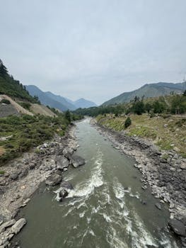 Breathtaking view of a river flowing through lush green mountainous landscape under a cloudy sky.