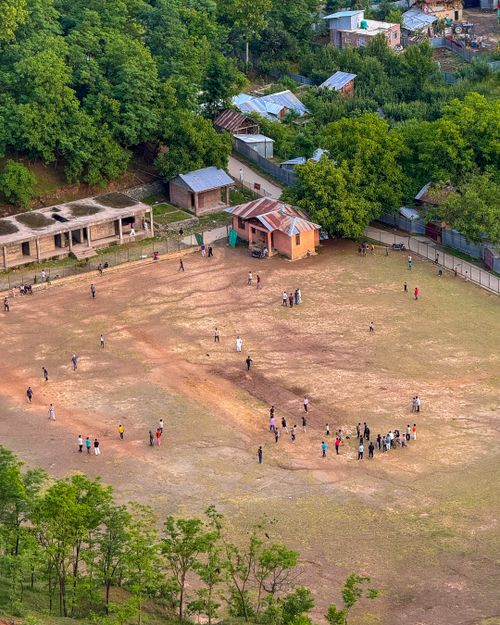 Free A captivating aerial shot of a group of people playing and socializing on a rural sports field surrounded by greenery. Stock Photo