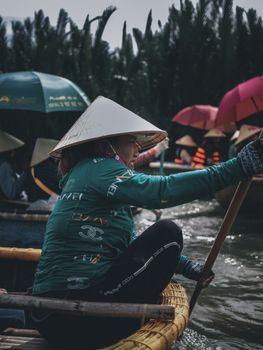 阳光明媚的日子里，一位戴着圆锥形帽子的女人在河上划着木制独木舟