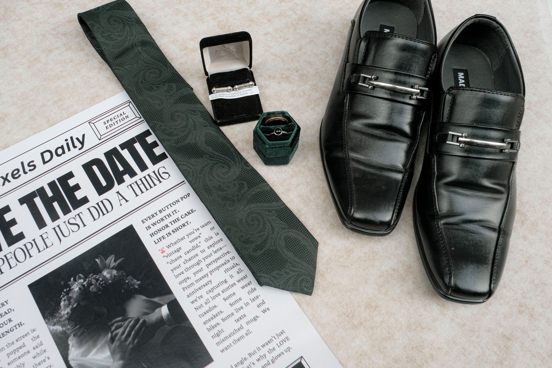 Flat lay of wedding essentials with shoes, tie, newspaper, and rings.