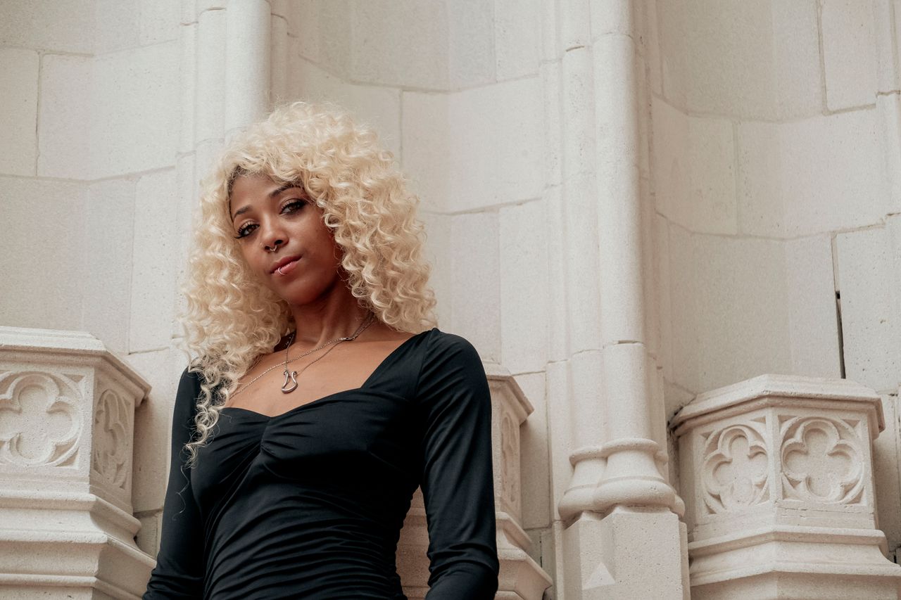 Woman with blonde curls in a black dress standing by stone architecture