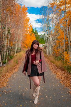 A woman walks down a leafy autumn road in Breckenridge, Colorado, showcasing fall fashion.