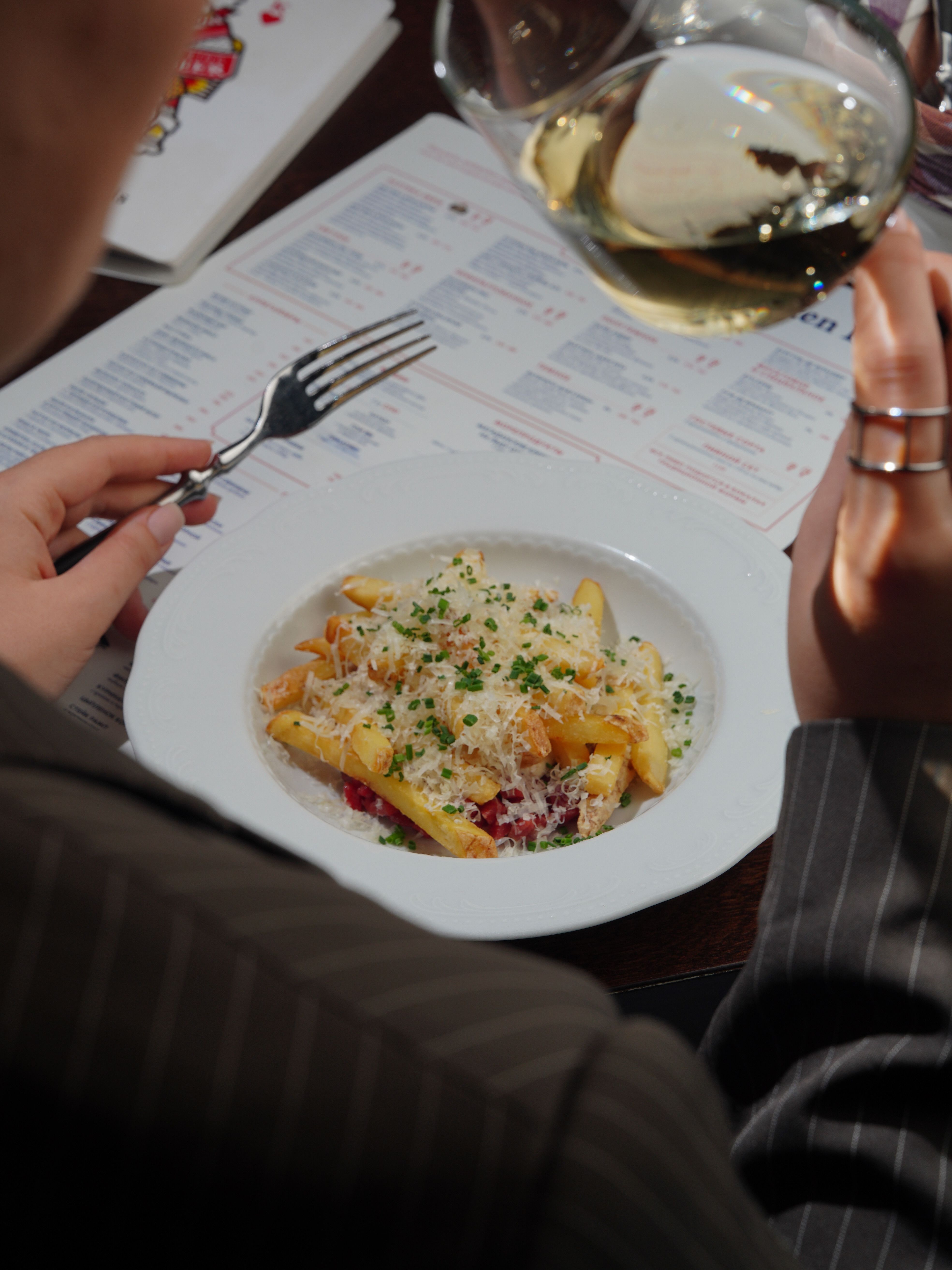 A detailed close-up of a gourmet pasta dish paired with white wine, set beside a dining menu.