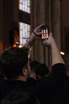 A person photographs stained glass windows inside a dimly-lit church, creating a contrast of light and shadow.