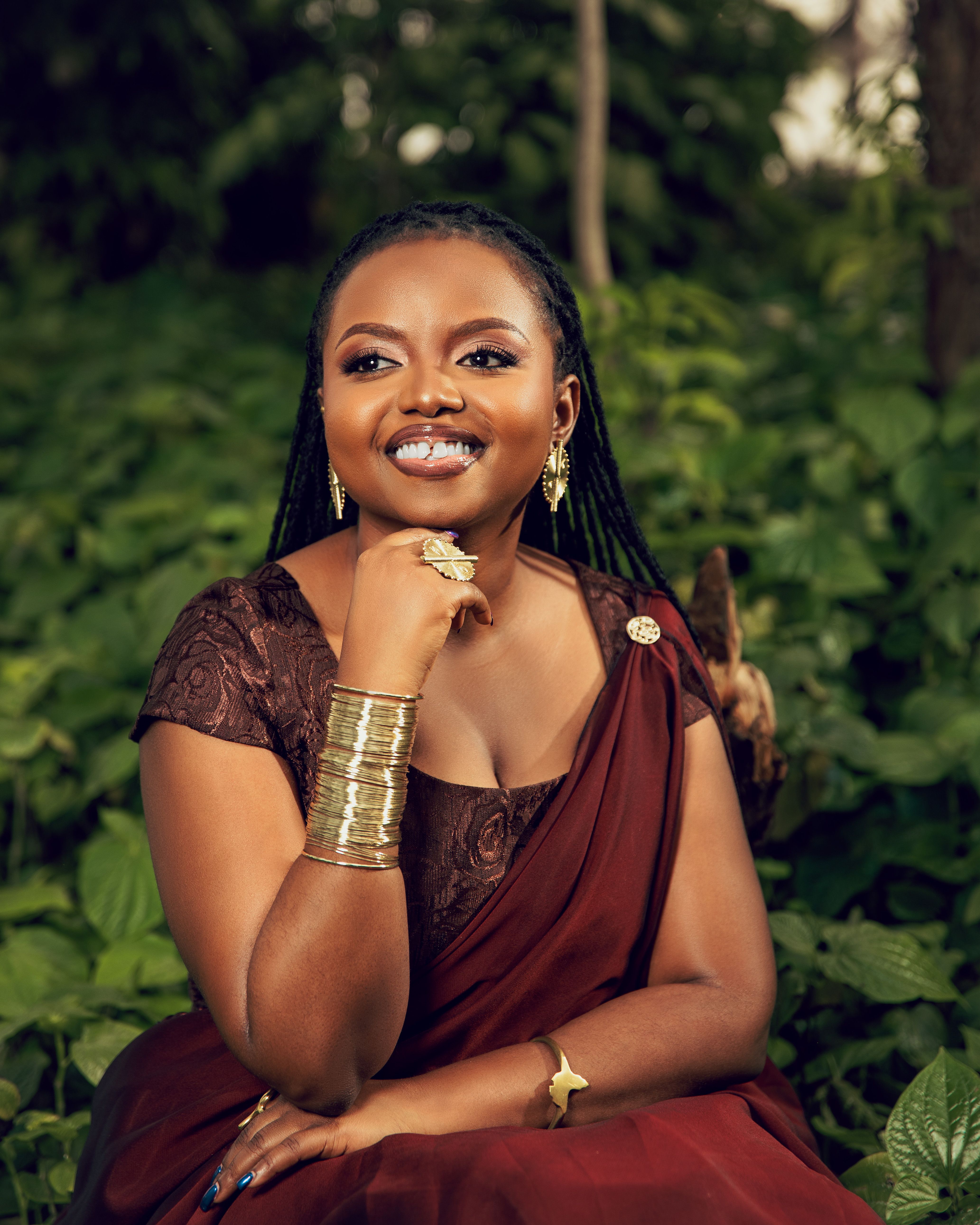 Portrait of a smiling woman in a brown dress surrounded by lush greenery.