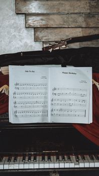 A vintage piano with sheet music for 'Ode to Joy' and 'Happy Birthday' in an artistic setting.