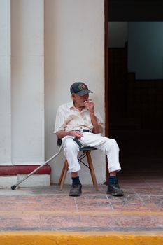 An elderly man sits on a chair outside in San Francisco de Campeche, capturing a moment of daily life.