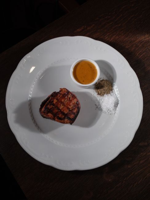 A toasted kaiser bun piled high with thin-sliced roast beef and melted cheese, next to a small cup of au jus for dipping.