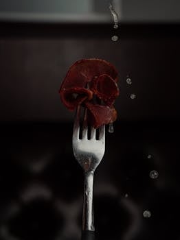 Creative shot of cured meat on a fork with dynamic water droplets.