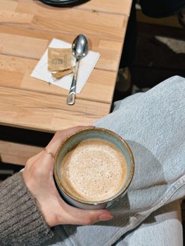 Overhead view of a cappuccino on someone's lap in a cozy café setting.