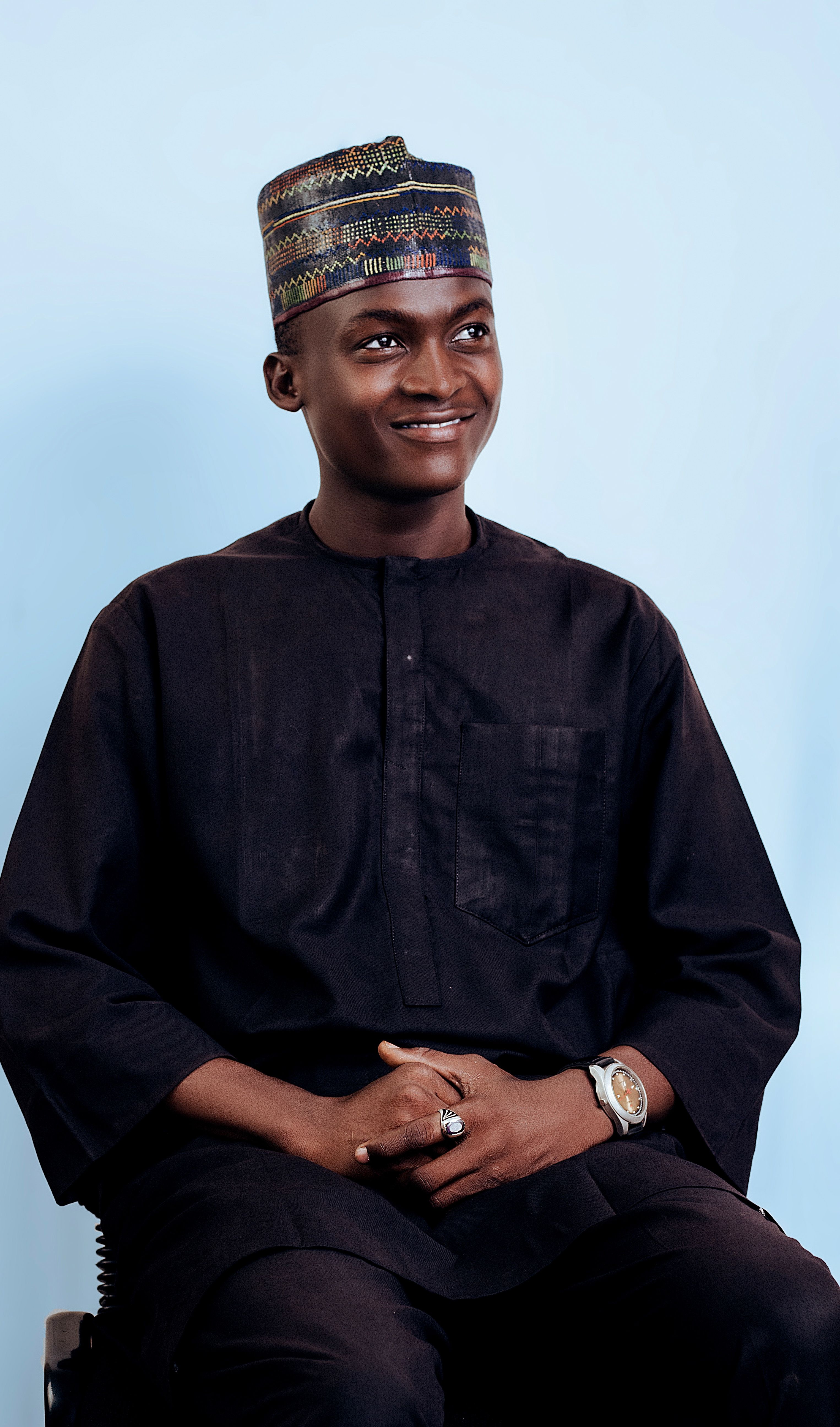 Portrait of a smiling man wearing traditional Nigerian clothing, captured indoors with a light blue background.