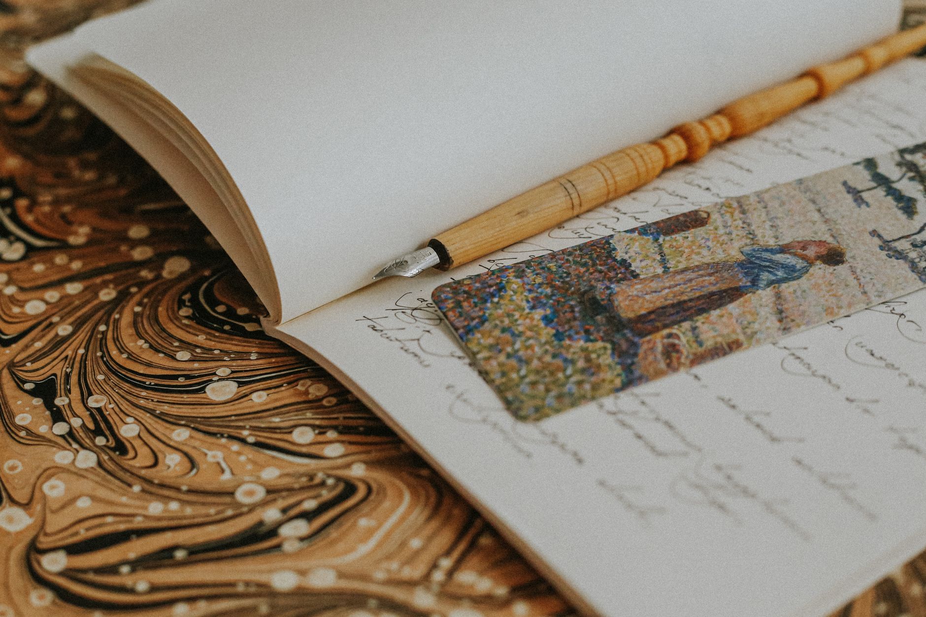 An artistic photo of an open notebook with a fountain pen and artistic bookmark on a marbled background.