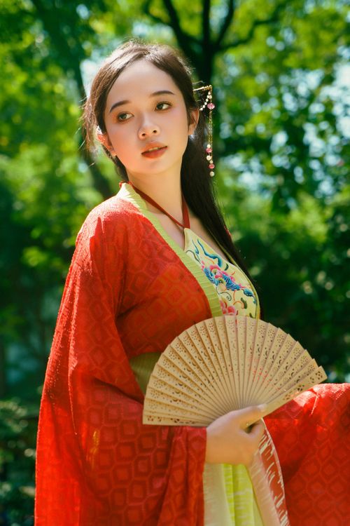Free A young woman in embroidered red attire and traditional Vietnamese costume holding a fan. Stock Photo
