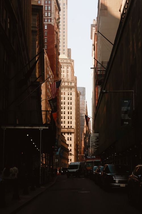 Free A vibrant New York City street scene at dusk with city flags and tall buildings framed by shadows. Stock Photo