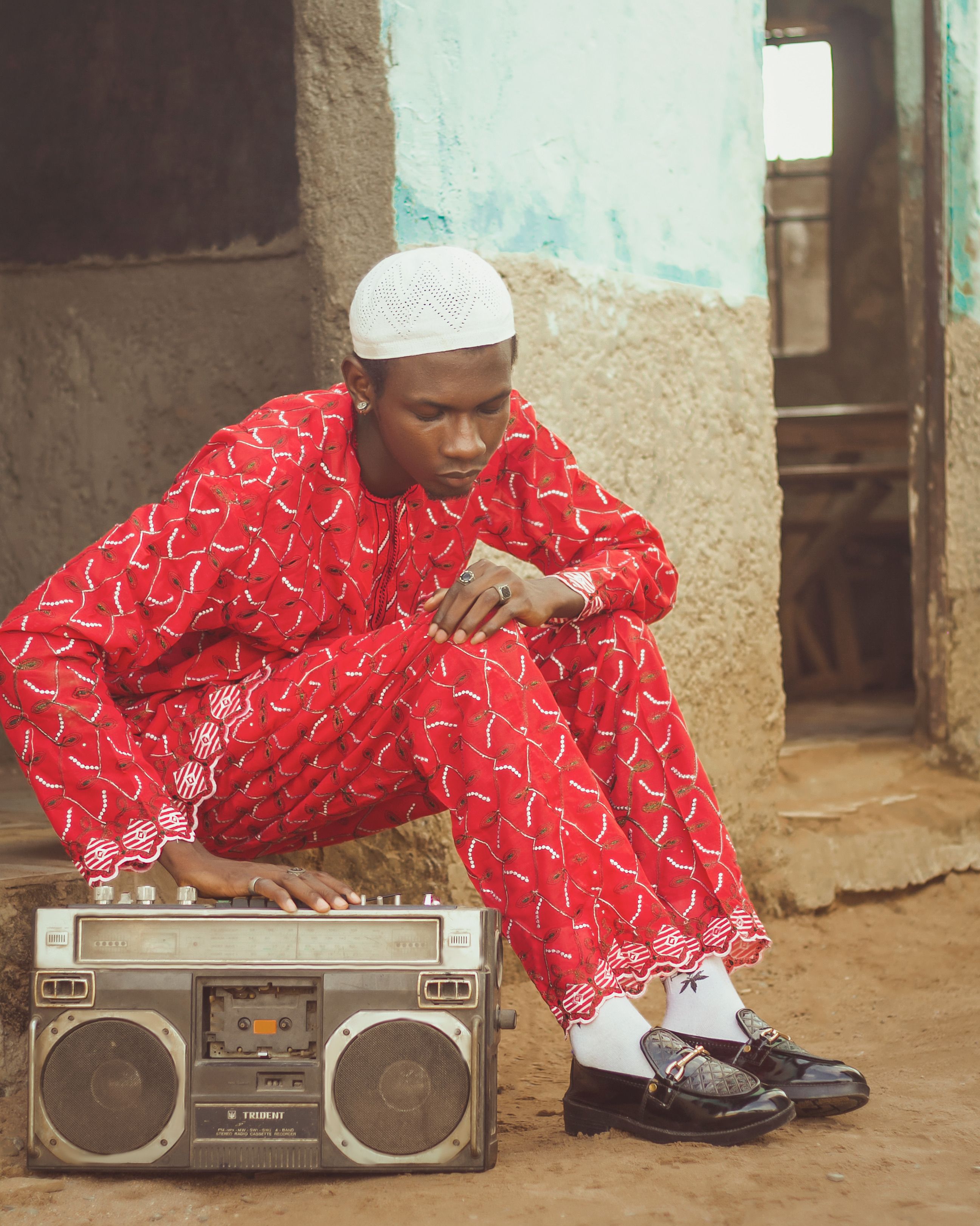 Stylish young man in vibrant red attire sits with a classic boombox in a rustic setting.