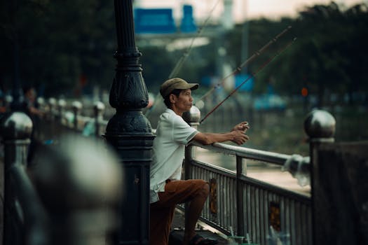 Photo by Văn Nguyễn Hoàng An adult man fishing along riverbank railing at twilight in an urban setting.