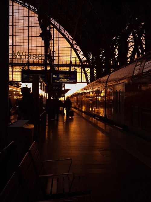 Free Travelers and a train silhouetted against a colorful sunset at a station. Stock Photo
