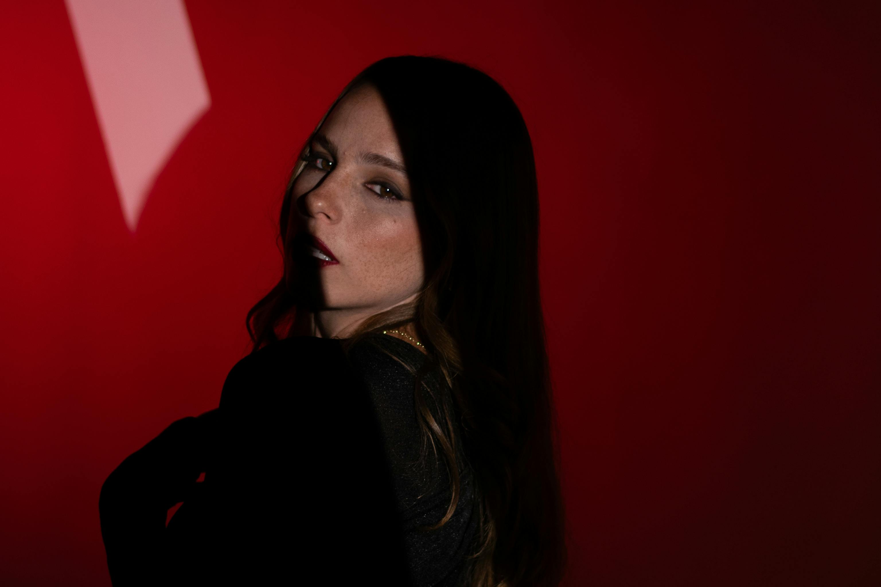 Artistic portrait of a woman in dim lighting with a striking red backdrop.