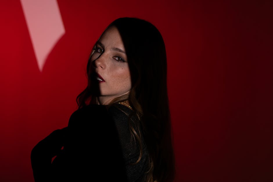 Artistic portrait of a woman in dim lighting with a striking red backdrop.