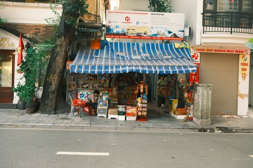 Free Colorful street vendor stall under a striped awning with various goods and a person seated inside. Stock Photo