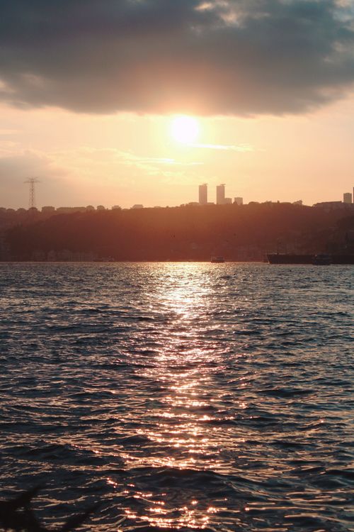 Free A captivating sunset reflecting on the waterfront with a distant city skyline. Stock Photo