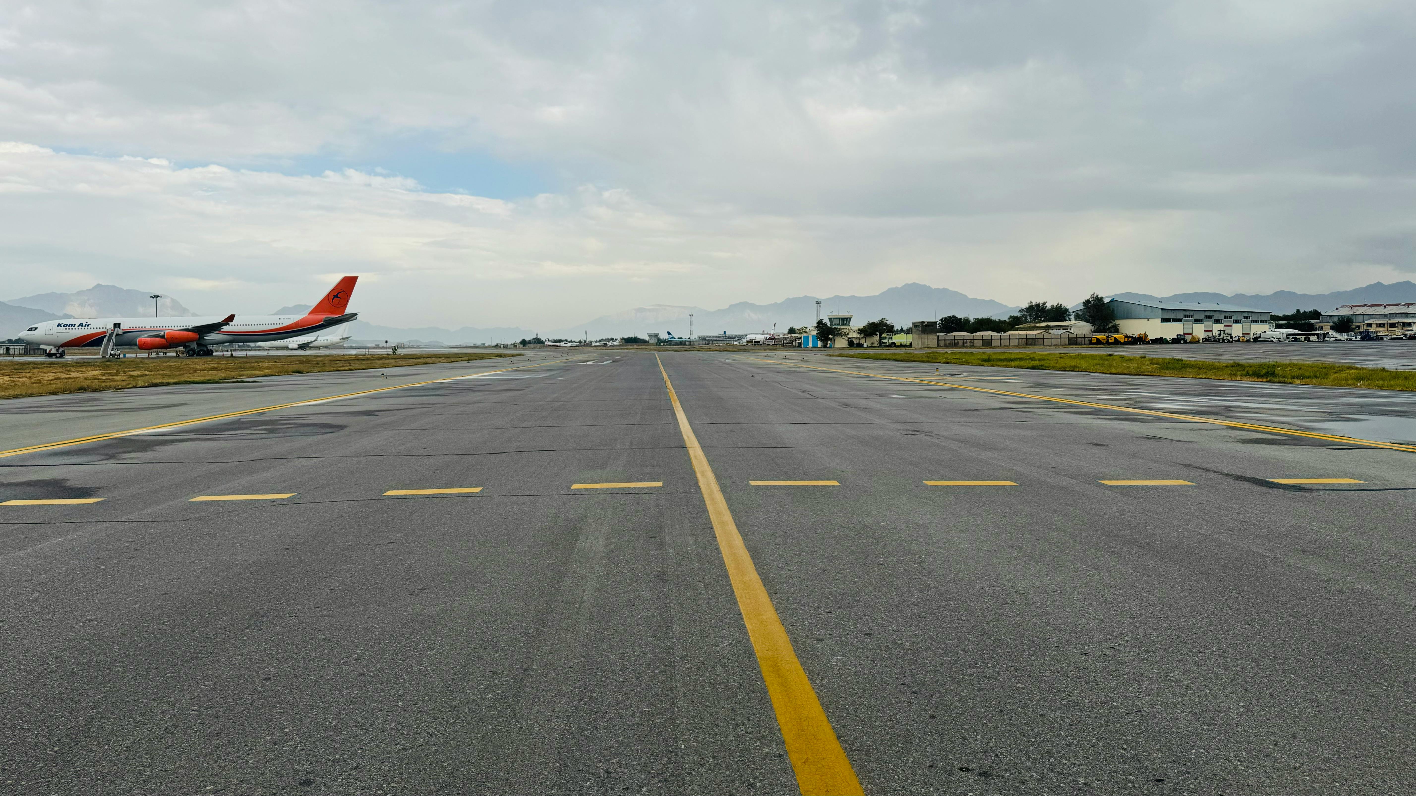 Empty runway at Kabul Airport with scenic mountain backdrop under a cloudy sky.