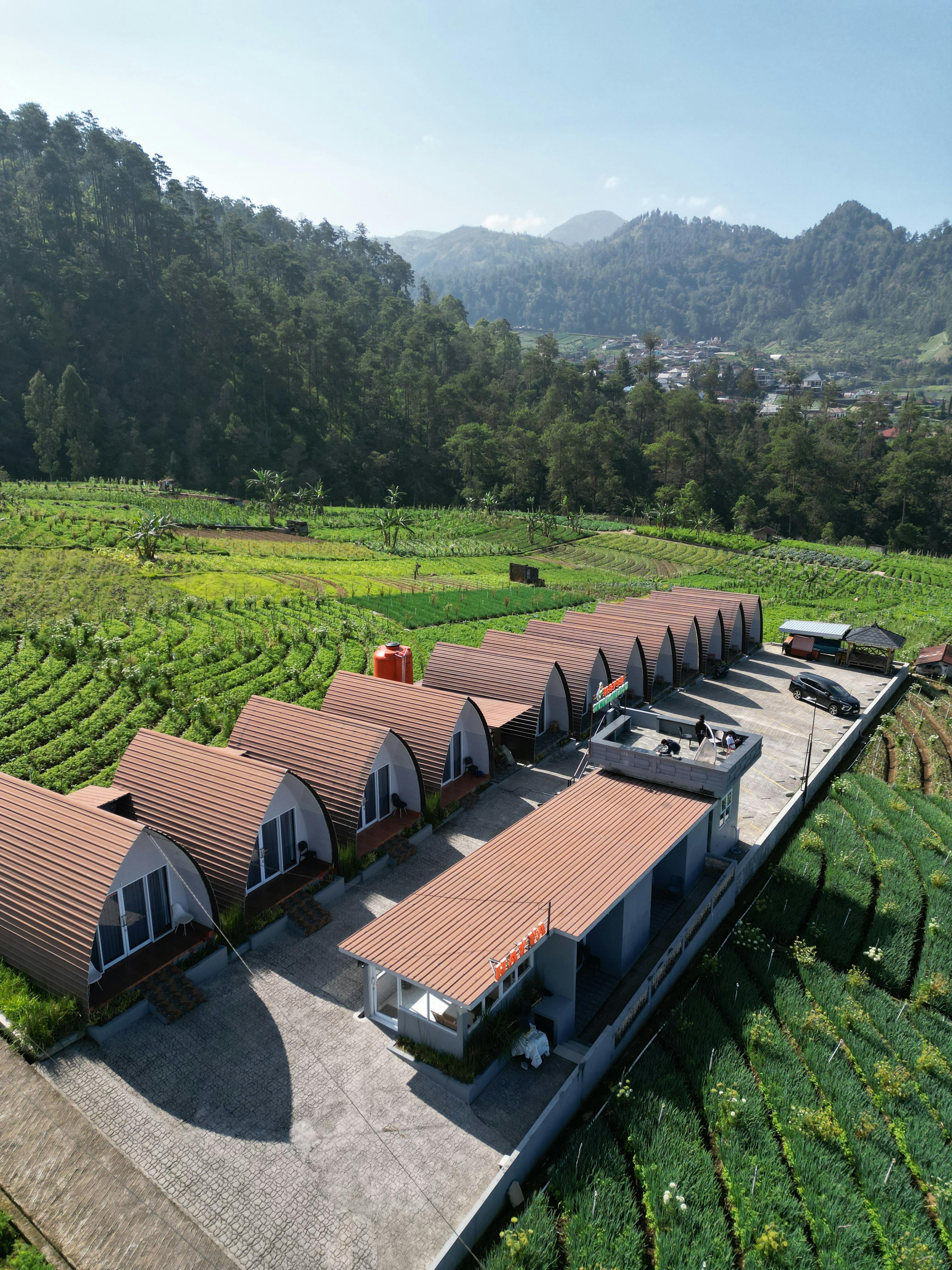 grátis Vista aérea de cabanas rústicas cercadas por colinas e montanhas verdejantes, destacando a arquitetura rural. Foto profissional