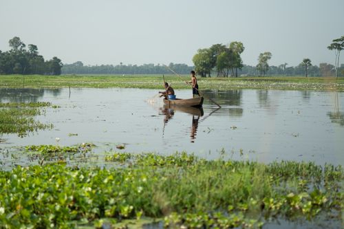 Free Two fishermen in a wooden boat fishing on a serene lake surrounded by lush greenery. Stock Photo