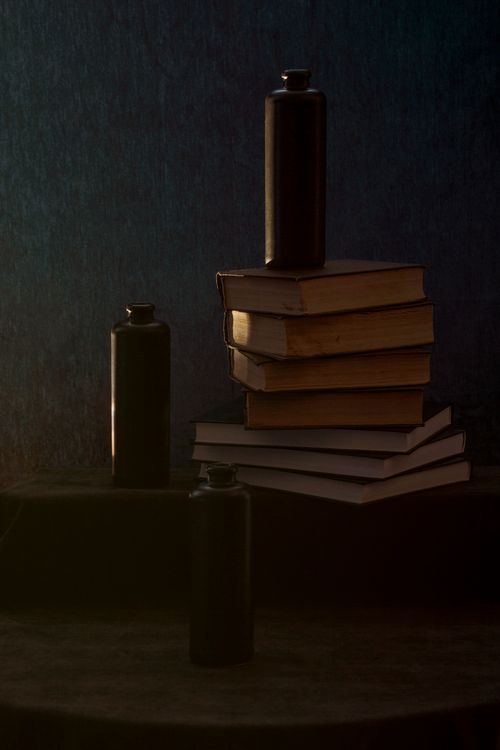 Free Moody still life featuring a stack of books and bottles against a dark background. Stock Photo