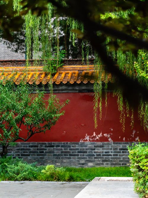 Free Scenic view of a traditional Chinese garden featuring a red wall, lush greenery, and classic architecture. Stock Photo