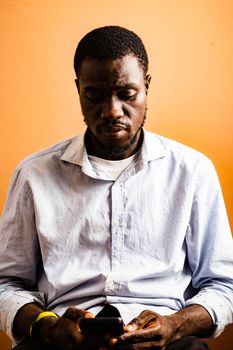 Portrait of an African man in Ghana using a smartphone against a warm orange background.
