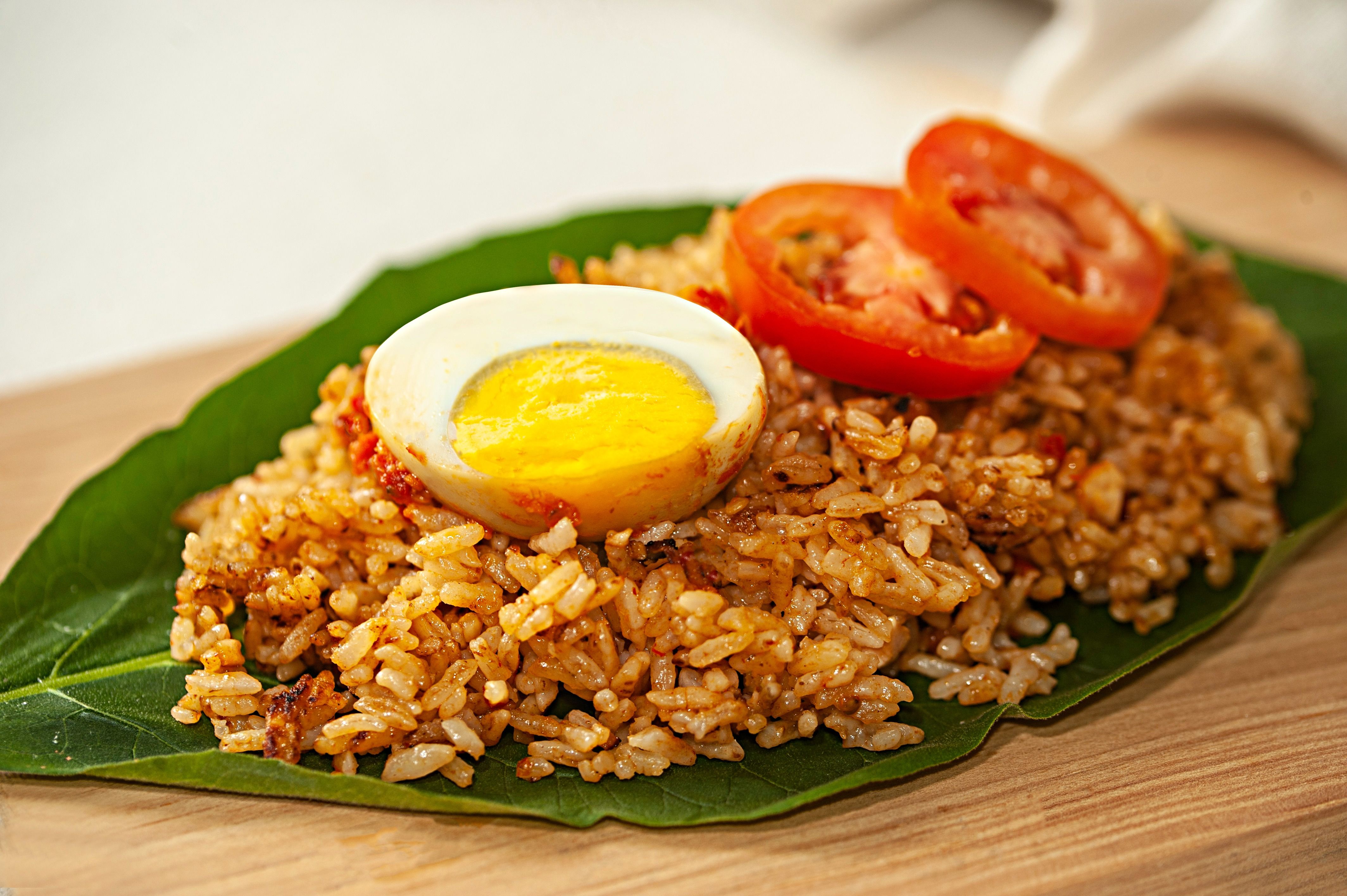 Close-up of spicy fried rice served on a leaf, topped with egg and tomato.