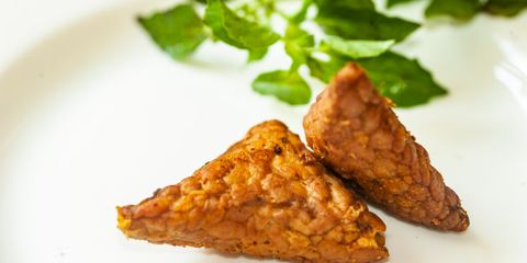Close-up of crispy fried tempeh served on a plate with fresh herbs.