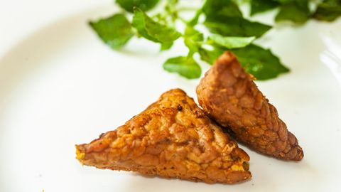 Close-up of crispy fried tempeh served on a plate with fresh herbs.