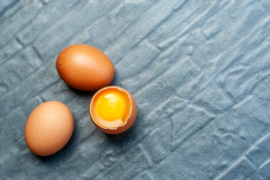 Close-up of three brown eggs on textured blue fabric; one egg is cracked open revealing the yolk.
