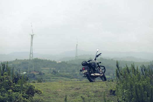 A classic motorcycle parked on a grassy hill with wind turbines in the backdrop, creating a serene countryside scene.