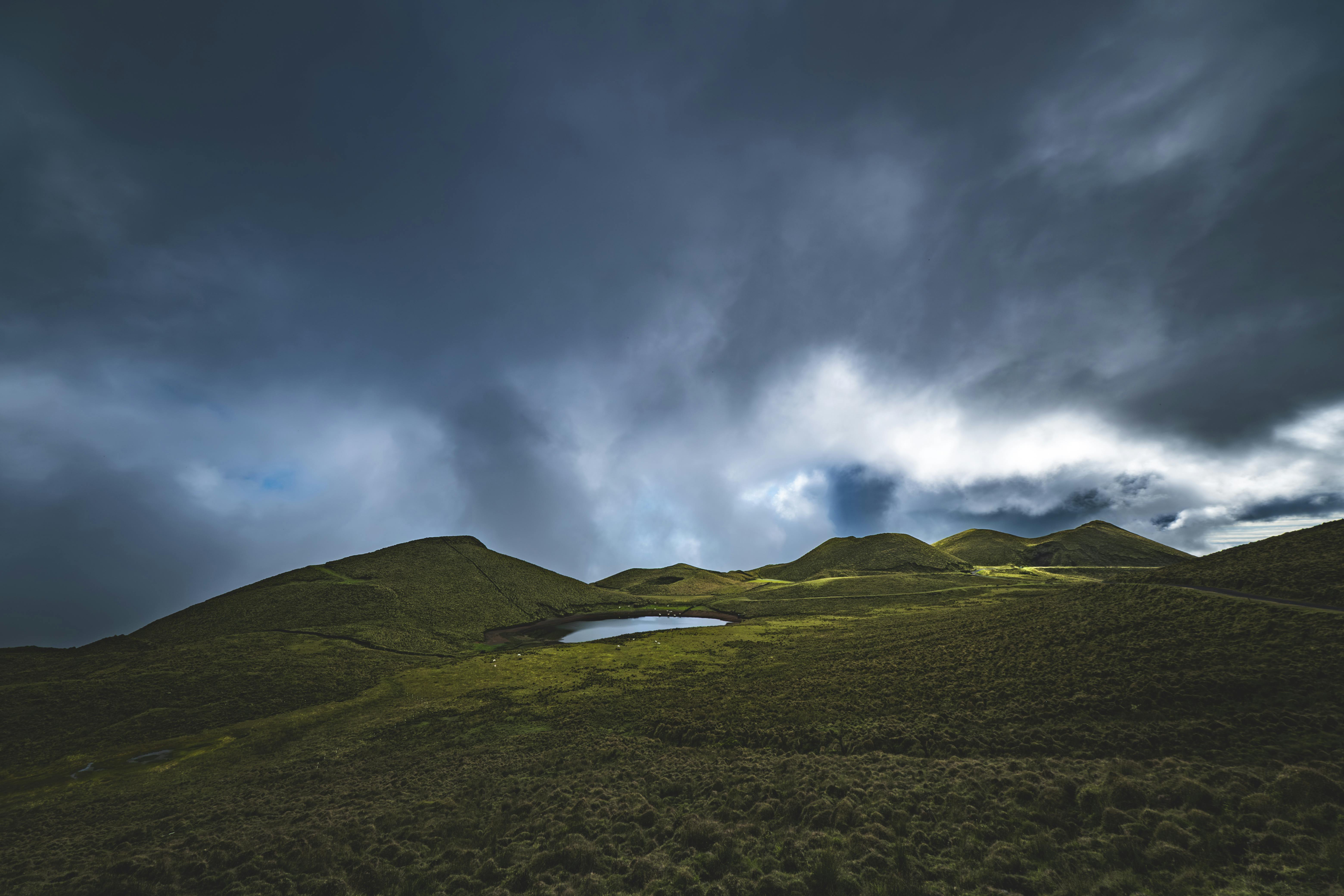 Paisagem dramática com colinas verdes e céu nublado, refletindo a construção rural.