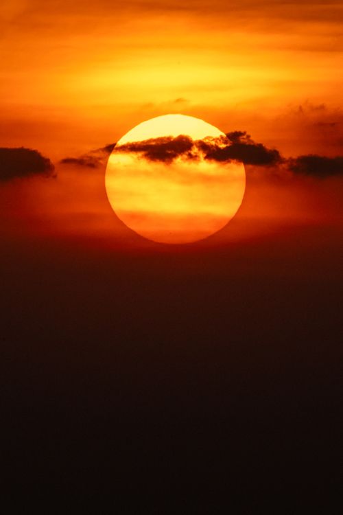 Free Captivating sunset with a vibrant orange sun and dark clouds. Stock Photo